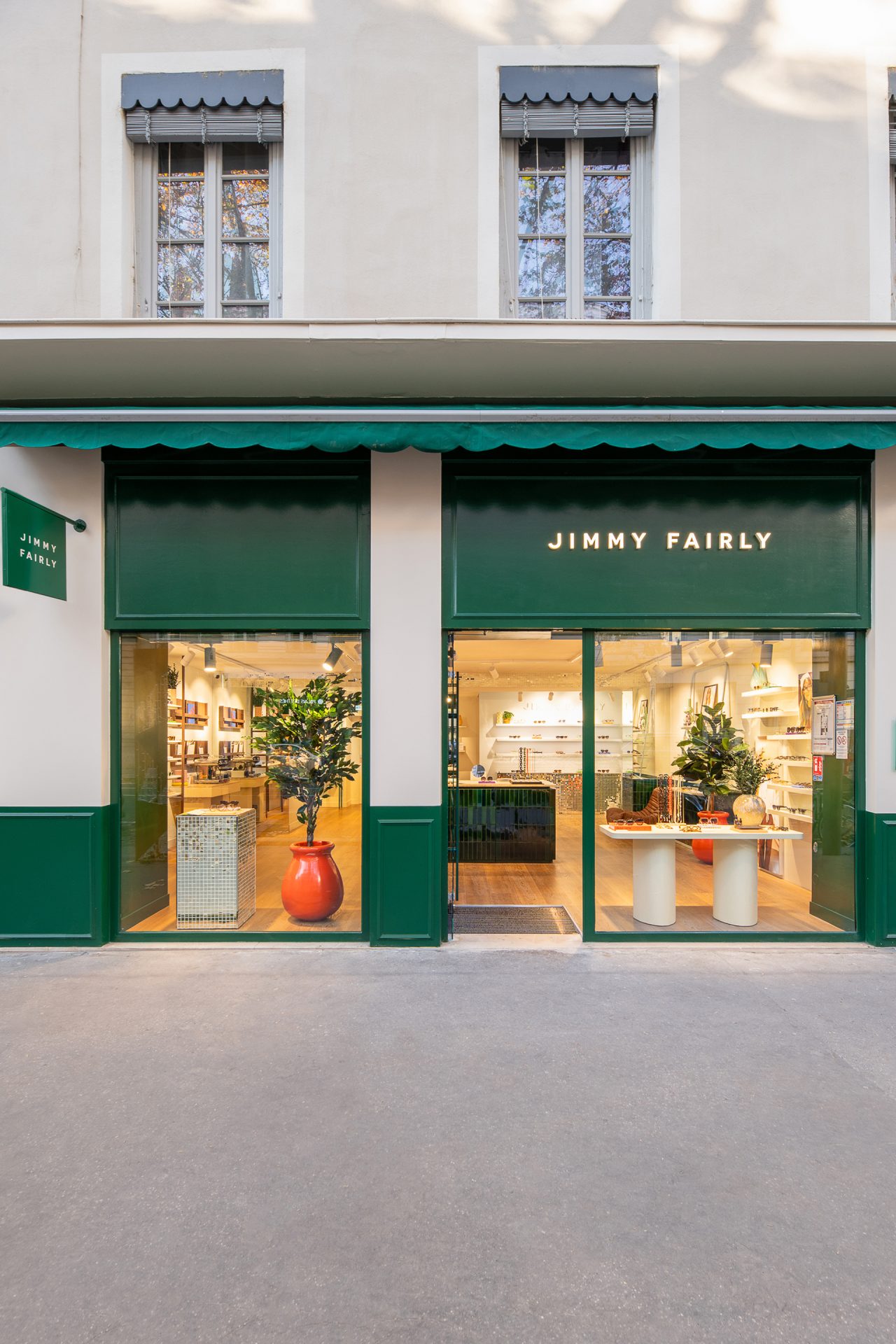 Façade entièrement verte de la boutique Jimmy Fairly de Lyon sur laquelle est fixé un store vert, une enseigne lumineuse et un drapeau.