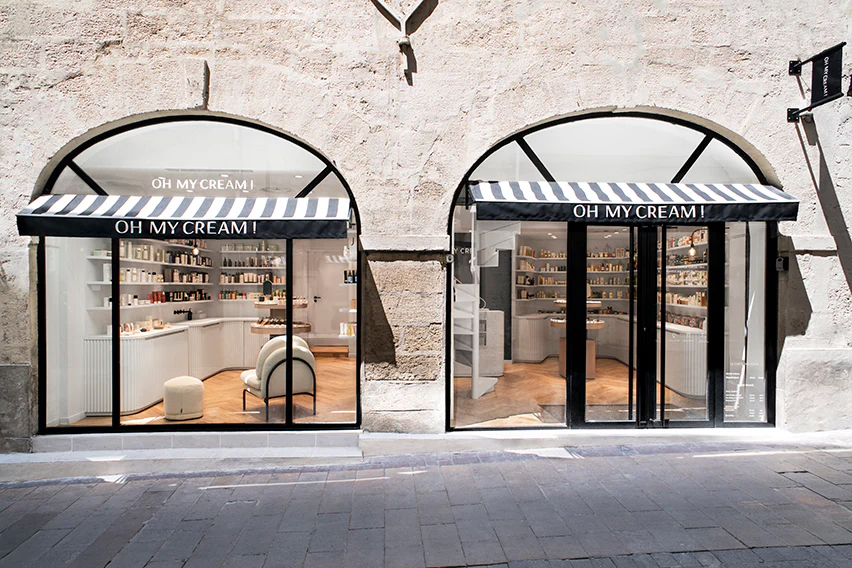 Façade en pierre avec deux grandes fenêtres cintrées, des stores rayés sérigraphié du nom Oh My Cream ! à Montpellier.