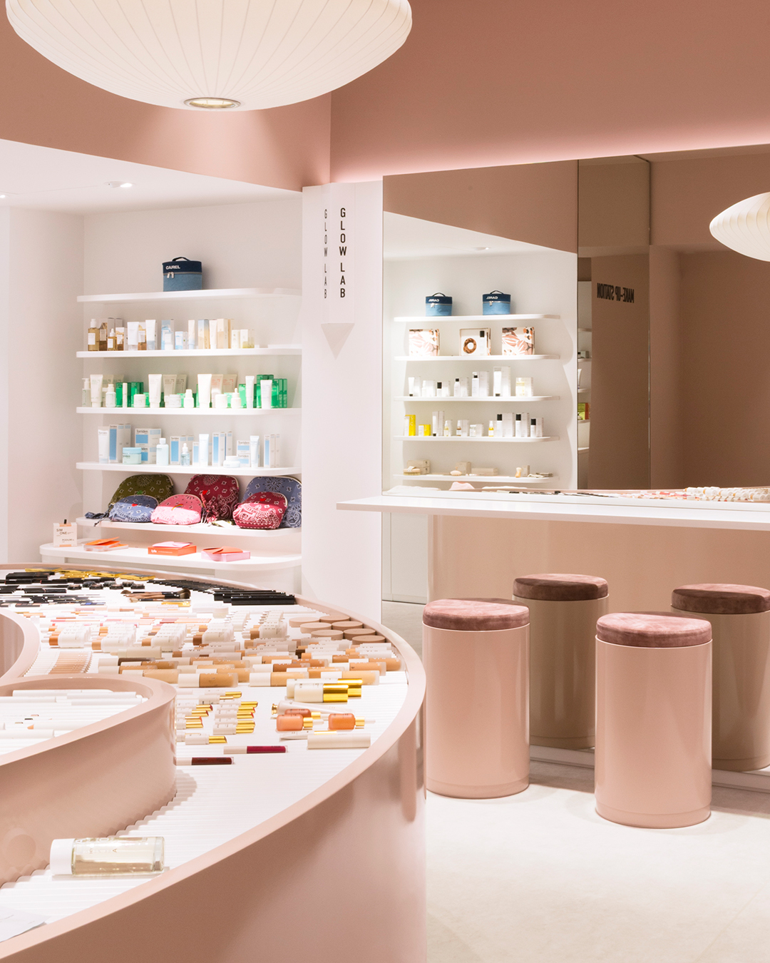 Intérieur moderne avec comptoirs courbés, tabourets et étagères de soins, décor rose doux, dans la boutique Oh My Cream ! à Paris.