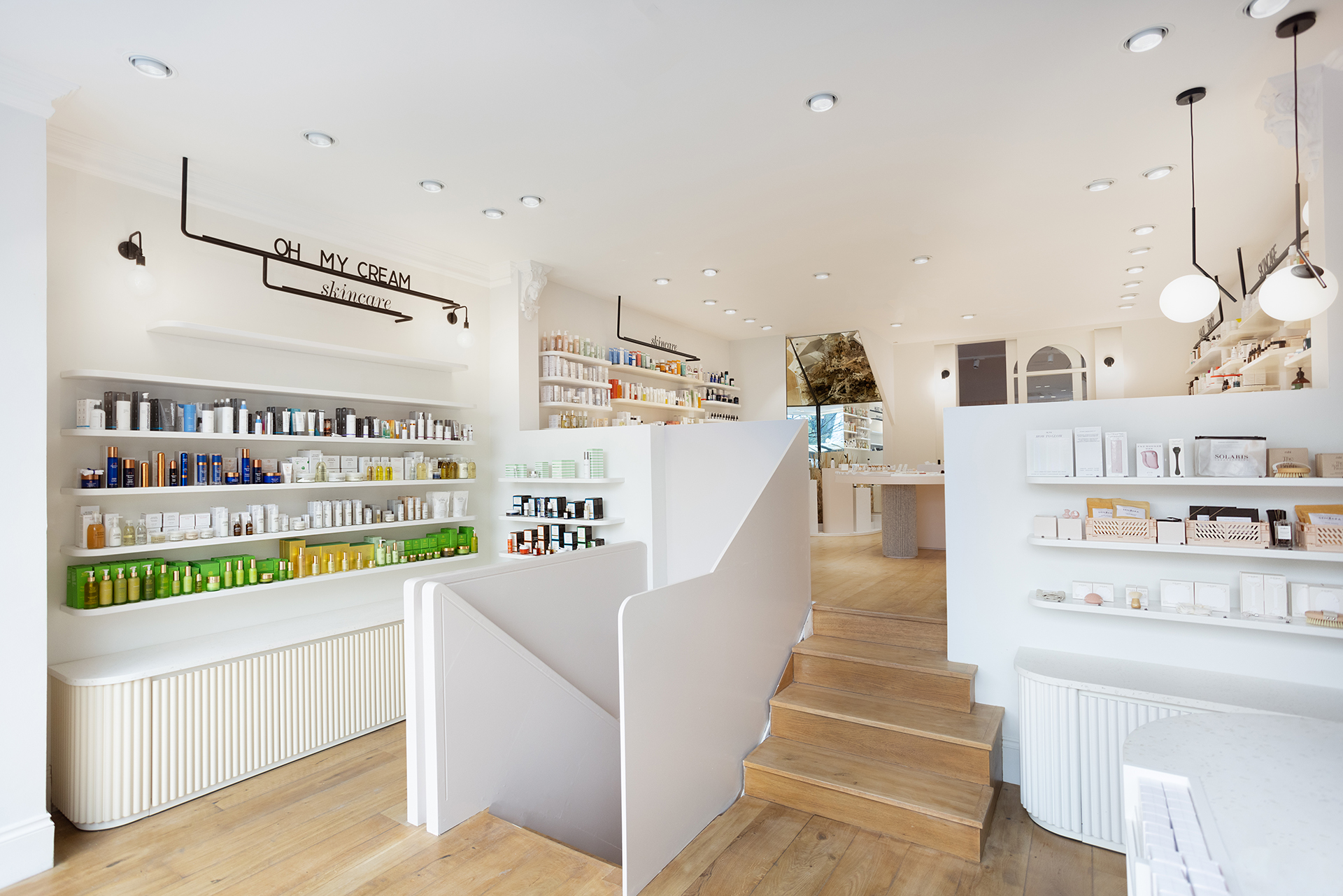 L'Intérieur lumineux et moderne avec étagères blanches, produits de beauté et escalier central en bois dans la boutique Oh My Cream ! de Westbourne.