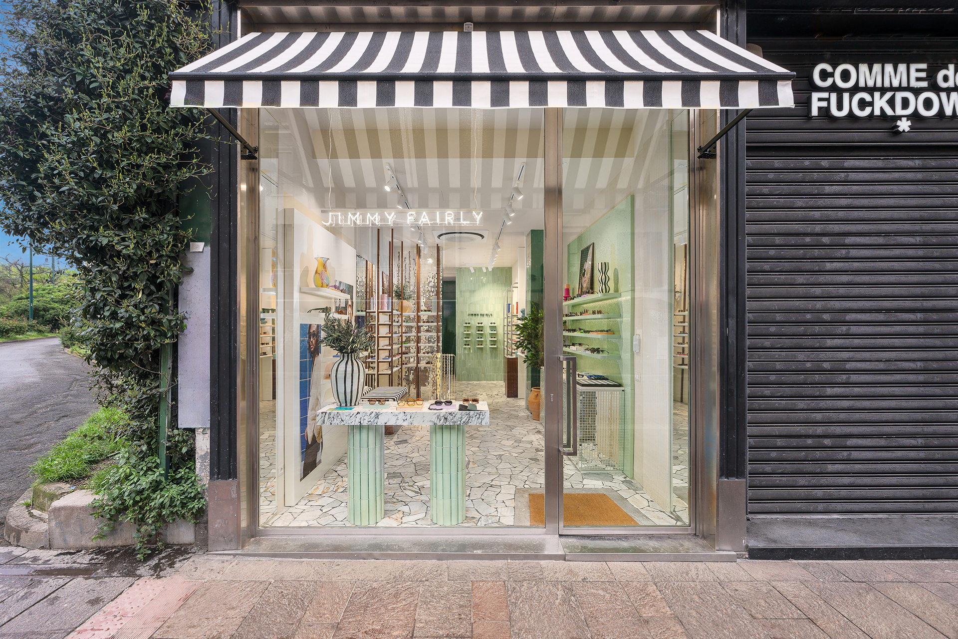 Façade avec enseigne Jimmy Fairly, porte vitrée, auvent rayé et lunettes exposées sur des tables dans la boutique de Porta Ticinese.