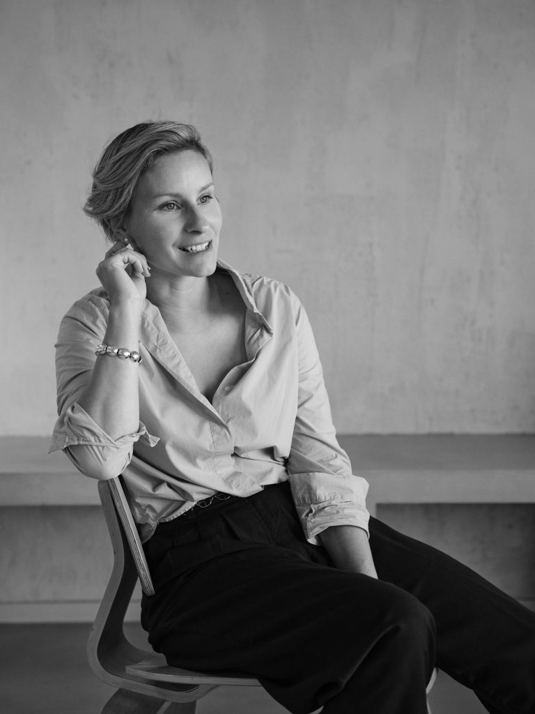 Intérieur sobre avec une femme souriante assise sur une chaise, pose naturelle, projet d'architecture retail de luxe.