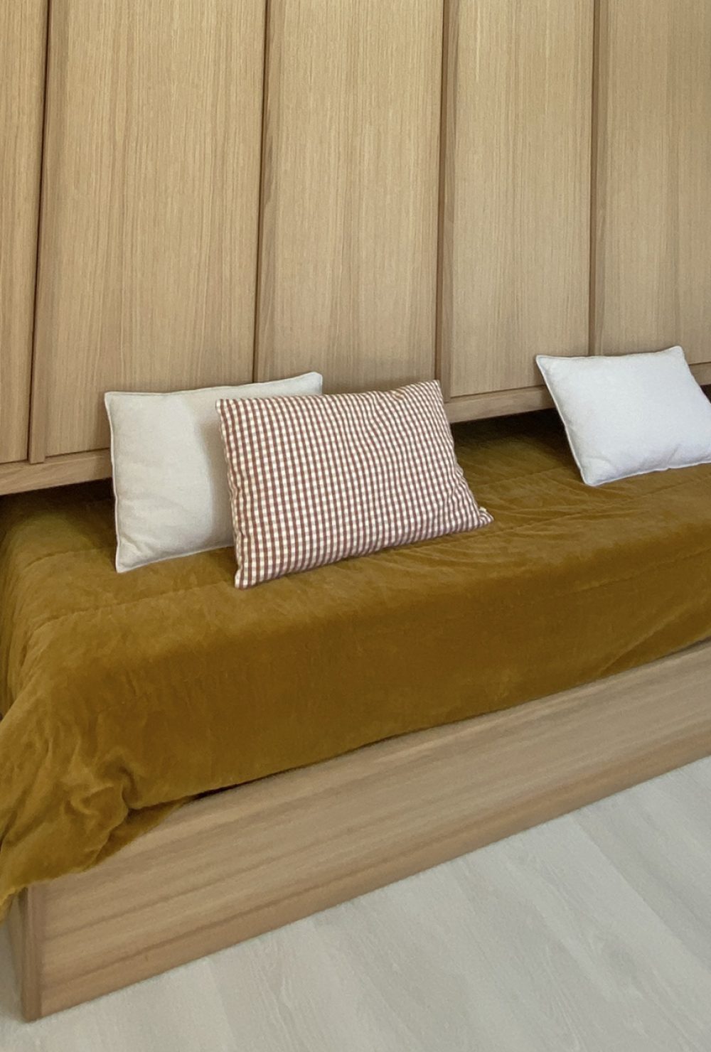 Intérieur clair avec un lit de jour en bois, couverture jaune moutarde et échelle en bois, projet d'architecture retail de luxe.