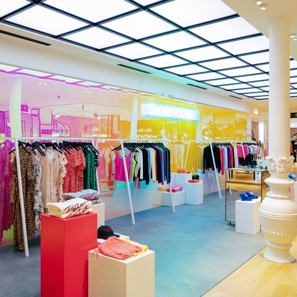 Intérieur avec mannequins, vêtements colorés sur des portants et sol en bois, éclairage néon vif, projet d'architecture retail de luxe.