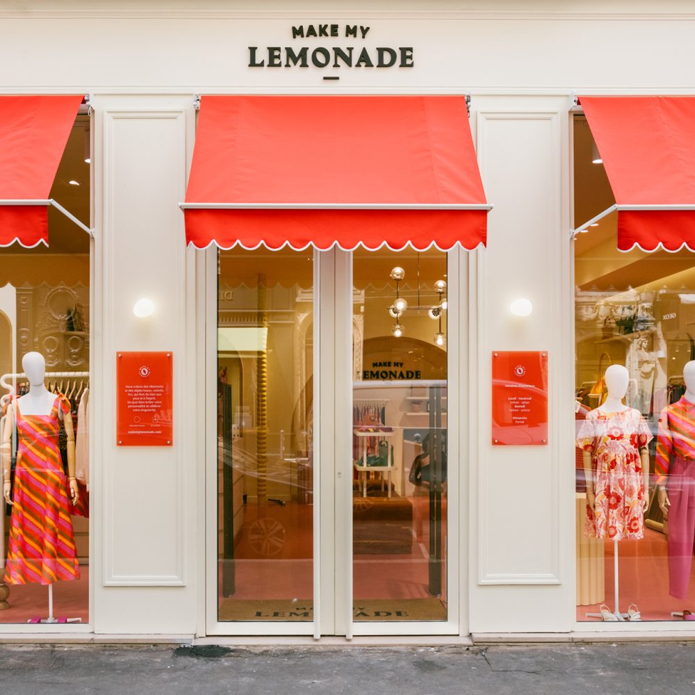 Façade crême avec des stores rouges au dessus des vitrines surplombées par l'enseign Make My Lemonade à Lyon.
