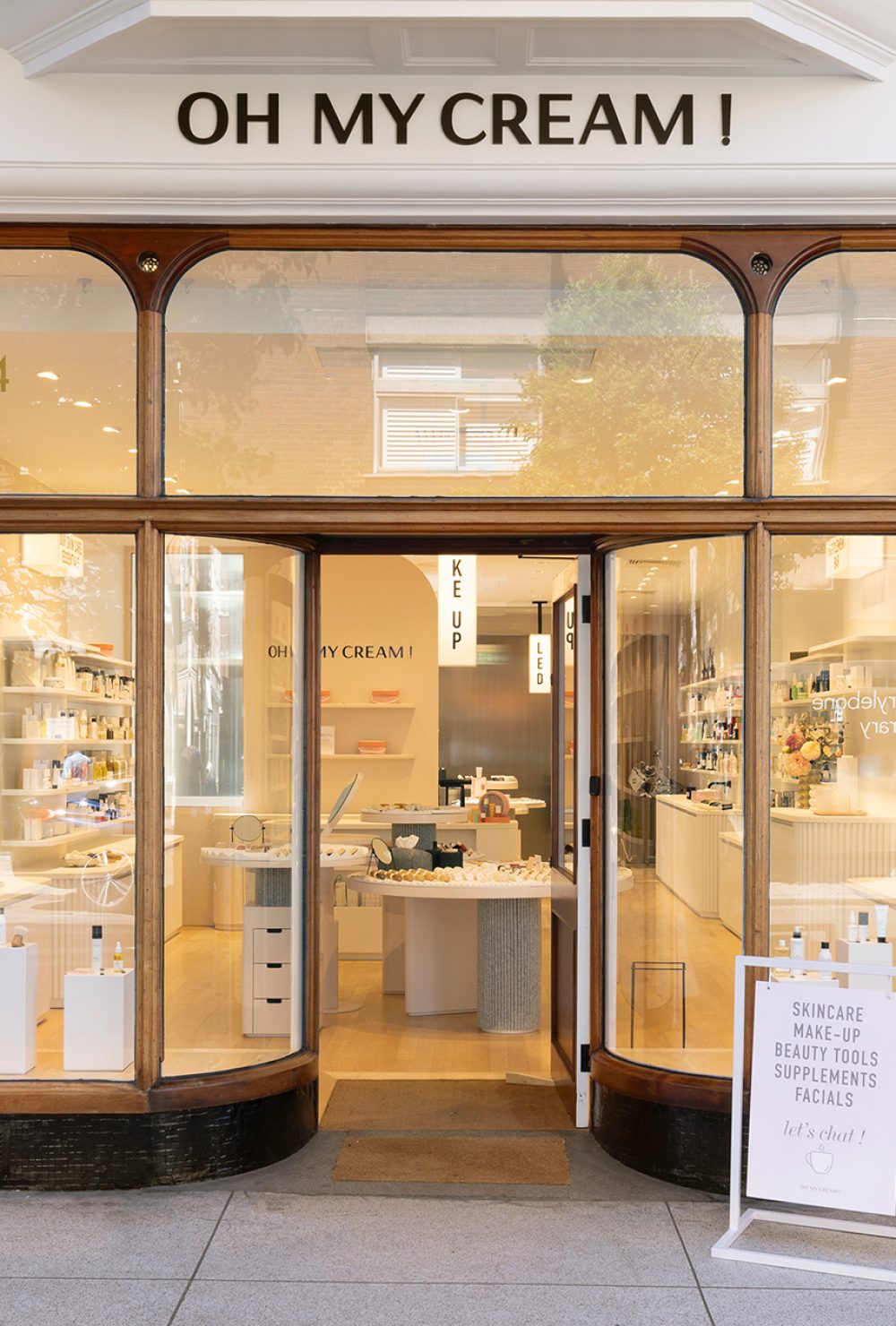 Façade avec grandes vitrines exposant des produits de beauté et un panneau sur le trottoir, dans la boutique Oh My Cream !.