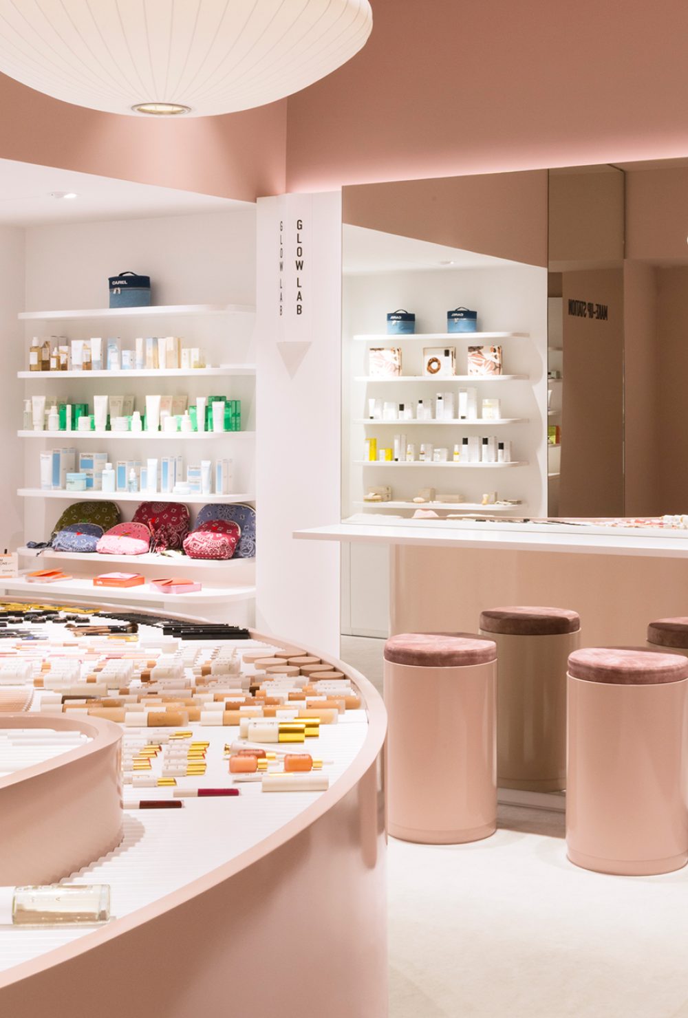 Intérieur moderne avec comptoirs courbés, tabourets et étagères de soins, décor rose doux, dans la boutique Oh My Cream ! à Paris.