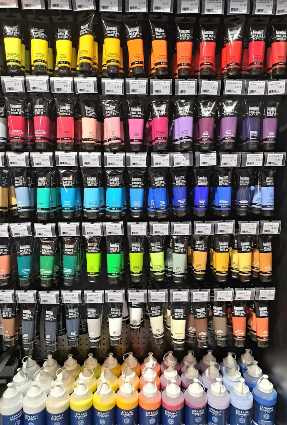 Rayonnage avec des tubes de peinture acrylique alignés sur les étagères dans la boutique Rougier&Plé Italie 2 de Paris.